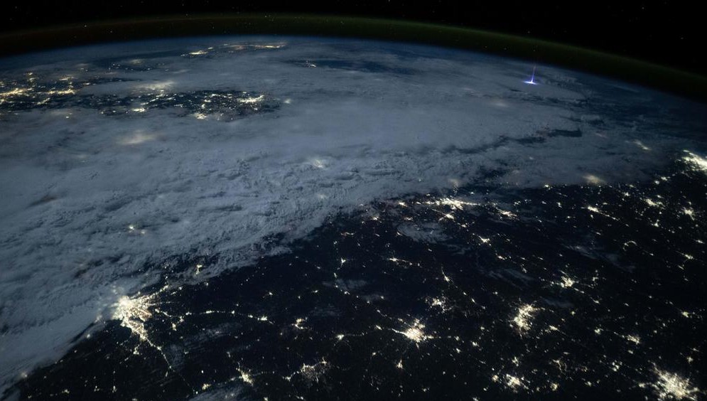 Fotografía de la Tierra desde el espacio mostrando un chorro gigante azul sobre una tormenta, con luces urbanas en la superficie. Imagen capturada por la NASA.